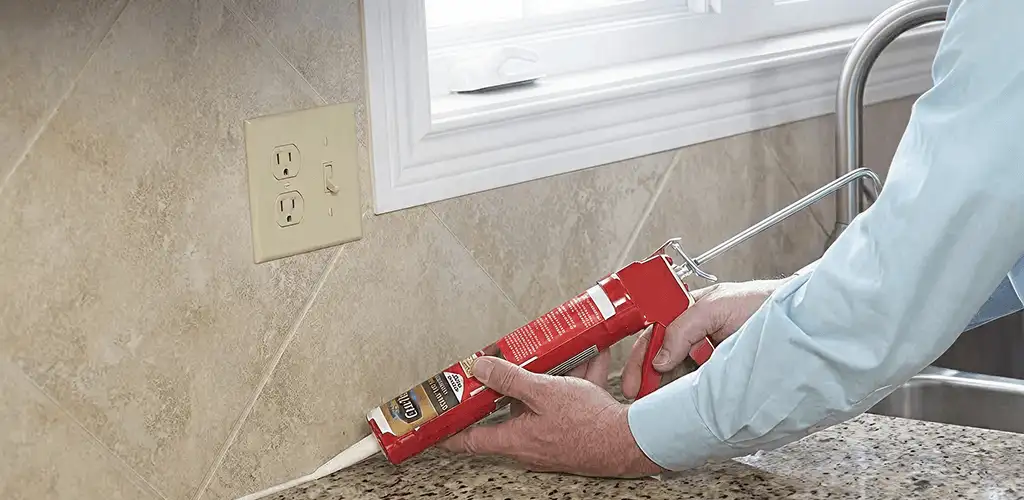 Handyman applying caulk along a kitchen backsplash and countertop seam in Grand Rapids, MI