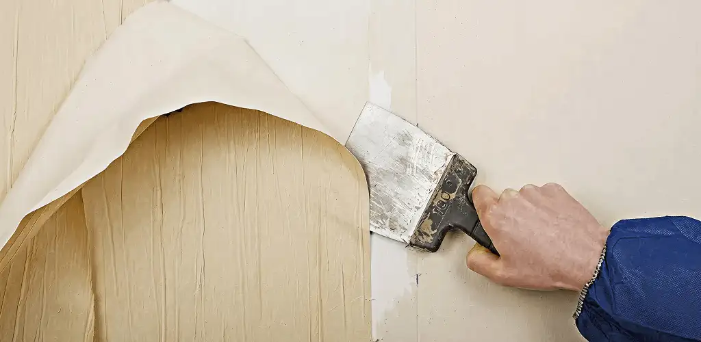 Handyman removing wallpaper with a scraper for wall preparation in Grand Rapids, MI